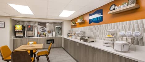 A modern kitchen area with a dining table and chairs, a coffee station, and a sign that reads "Welcome."