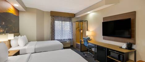 A hotel room with two beds, a desk, a TV, and a large window with patterned curtains.