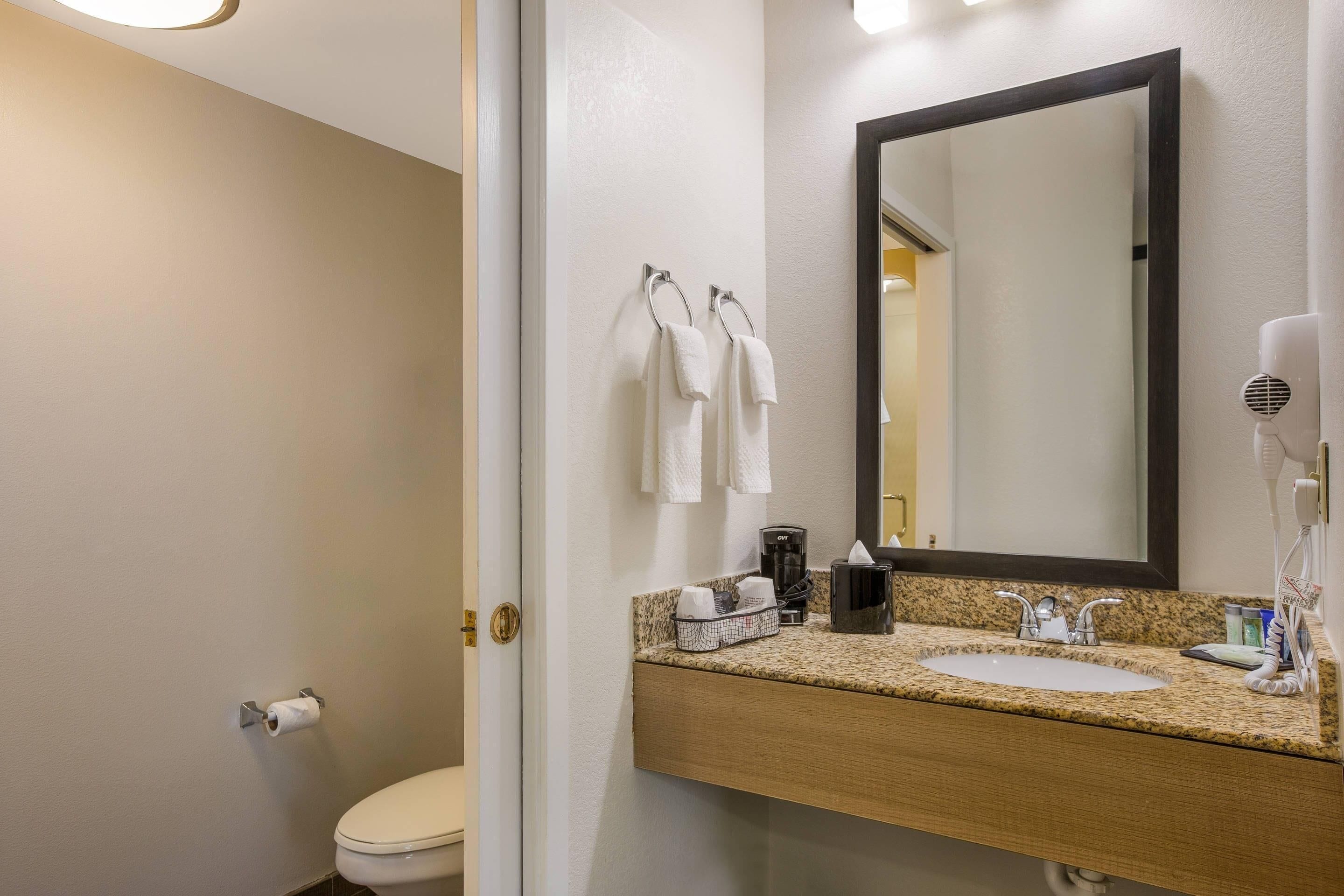 Un bagno d'albergo con lavandino, specchio, asciugamani e articoli da toilette.