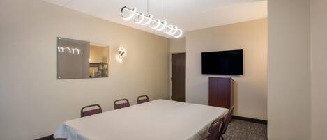 A conference room with a table, chairs, a flat-screen TV, and a ceiling-mounted light fixture.