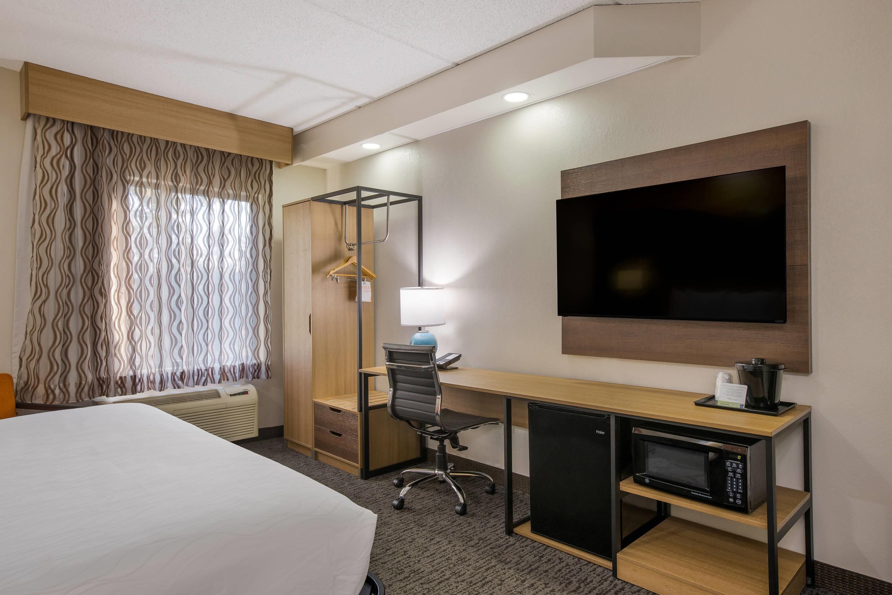 A hotel room with a bed, desk, chair, TV, and microwave.