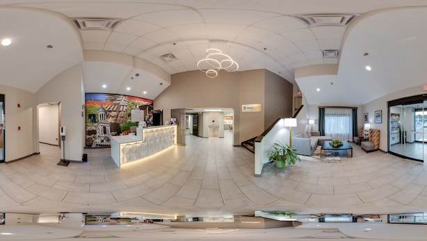 A modern hotel lobby with a reception desk, seating area, and a staircase leading to upper floors. - Clarion Pointe Sevierville-Pigeon Forge (Sevierville)
