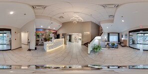 A modern hotel lobby with a reception desk, seating area, and a staircase leading to upper floors. - Clarion Pointe Sevierville-Pigeon Forge (Sevierville)