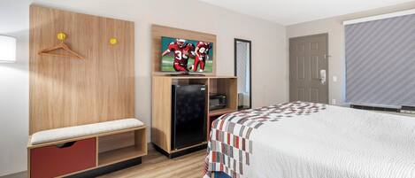 A hotel room with a bed, a desk with a computer, a wardrobe, a mirror, and a television.