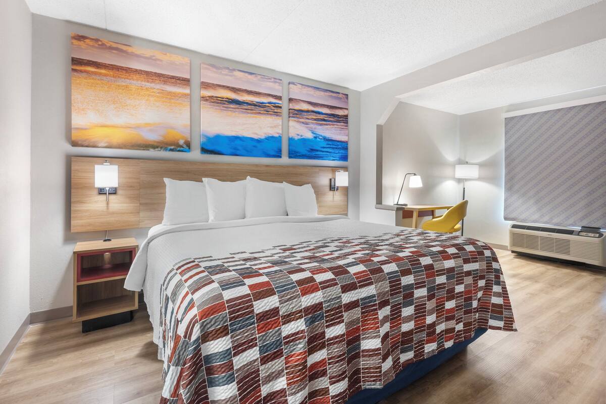 A modern hotel room with a large bed, a wooden headboard, two wall-mounted lamps, a yellow chair, and a large window with a view of the ocean.