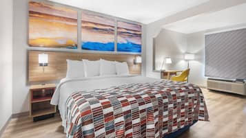 Camera d'albergo con un letto grande, un comodino, una scrivania, una sedia e una TV a parete.