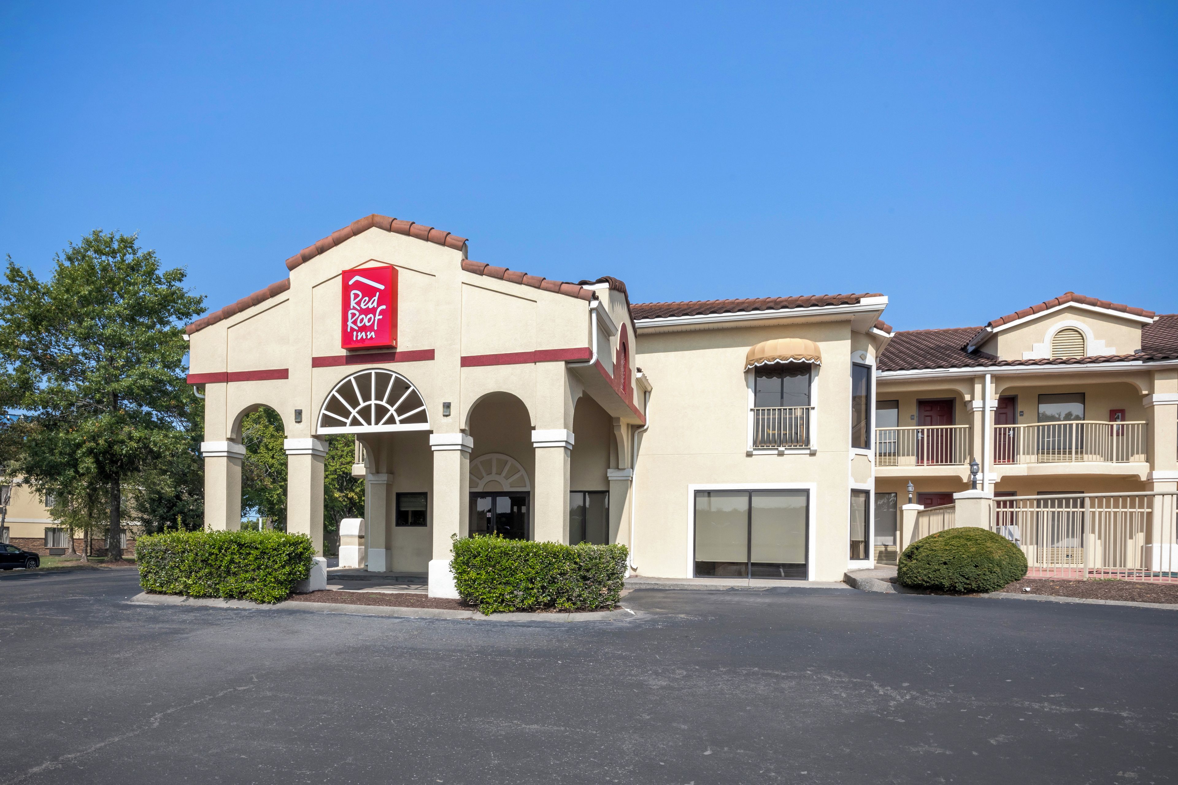 Un Red Roof Inn con un edificio de dos pisos, entrada arqueada y un balcón en el segundo piso.