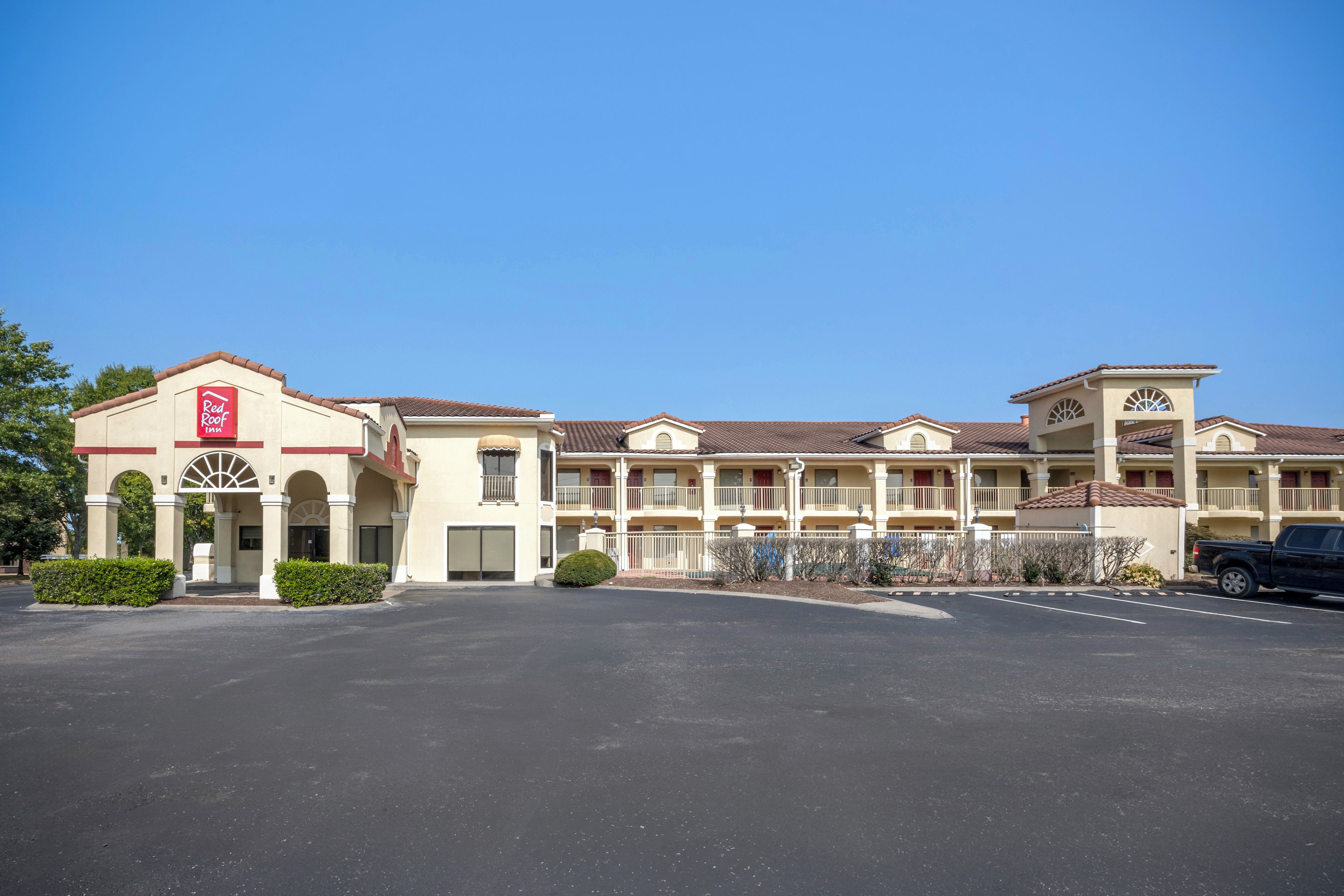 A hotel with a central entrance, multiple balconies, and a parking lot.