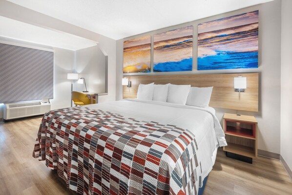 Ein Hotelzimmer mit einem großen Bett, einem hölzernen Kopfteil, einem Nachttisch, einer Lampe und einem an der Wand befestigten Kunstwerk.