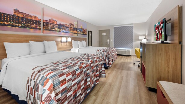 Une chambre d’hôtel avec un grand lit, un bureau, une télévision et un tableau représentant un paysage urbain accroché au mur.