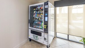 Un distributeur automatique proposant une variété de collations et de boissons, situé dans une pièce dont le sol est carrelé et qui possède une fenêtre donnant sur un paysage agréable.