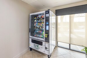 Ein Getränkeautomat mit verschiedenen Snacks und Getränken, in einem Raum mit Fliesenboden und einem Fenster mit Blick.