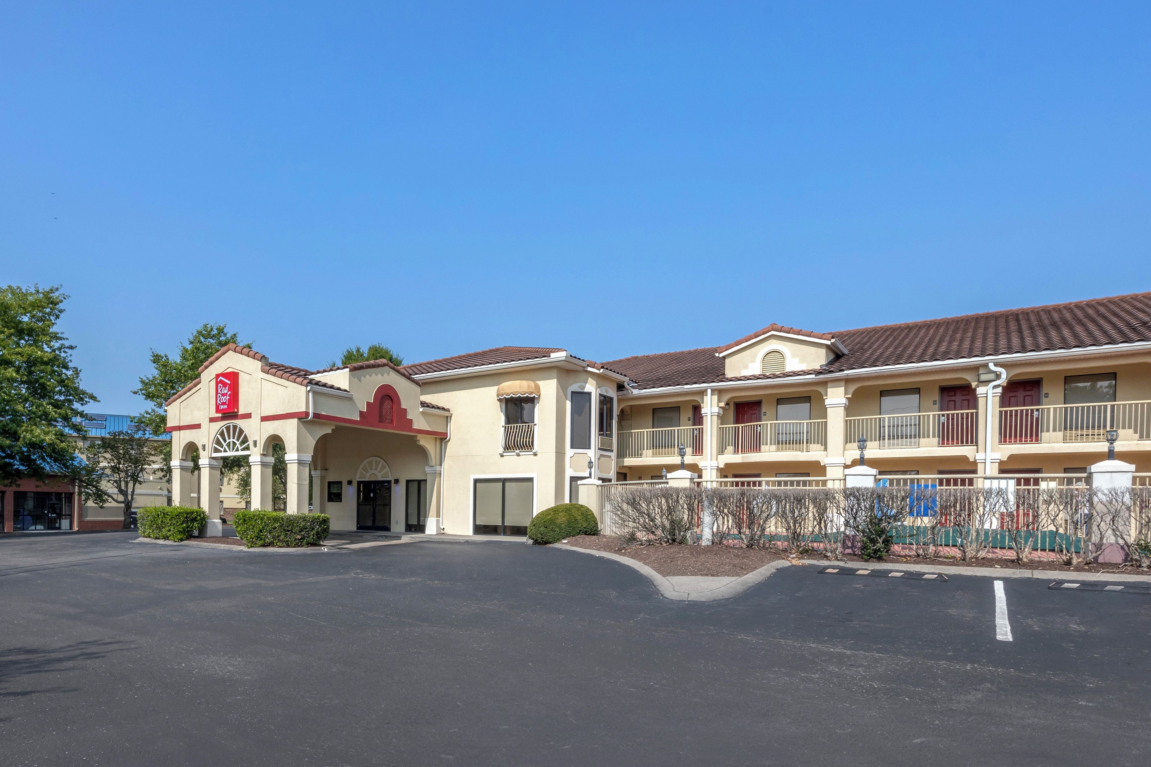 A hotel with a red roof sign, multiple balconies, and a parking lot.