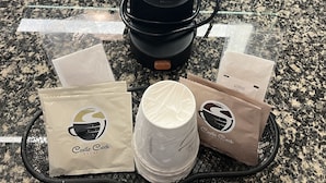 Une machine à café, des tasses à café et des sachets de café sont posés sur un plan de travail en granit.