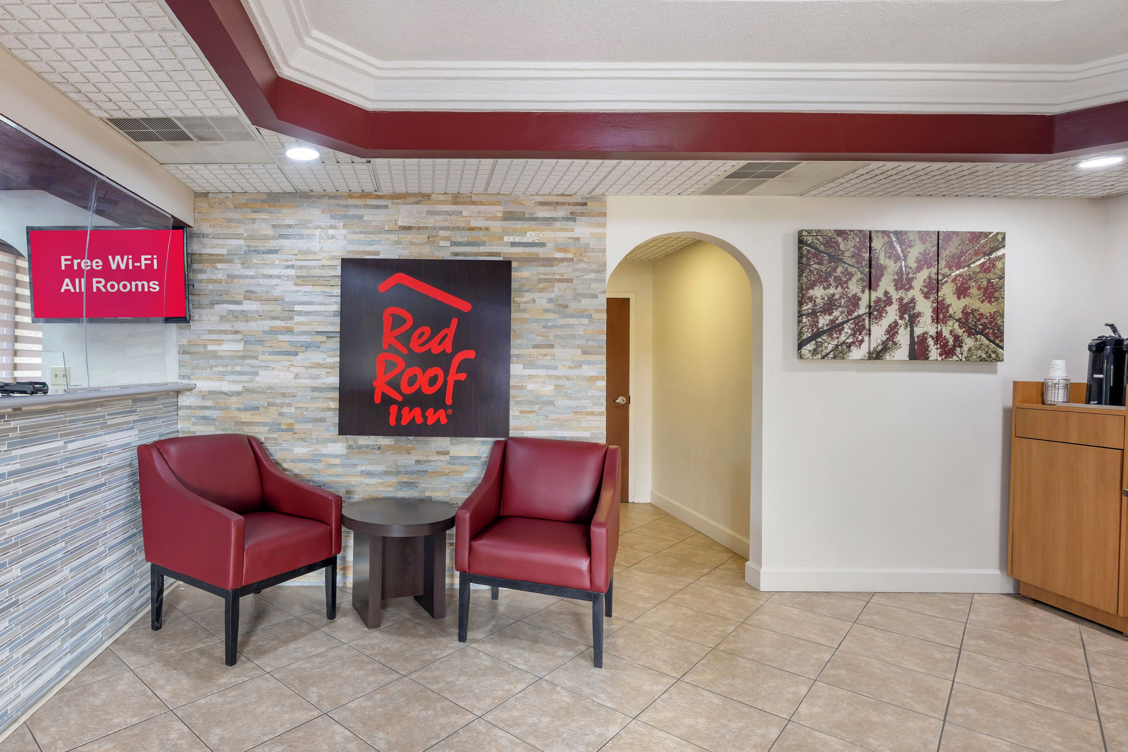 A Red Roof Inn reception area with a stone wall, two leather chairs, a small table, and a sign indicating free Wi-Fi in all rooms.