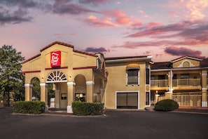 A Red Roof Inn with a traditional architectural style, featuring a prominent red sign, arched windows, and a balcony on the second floor.