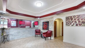 Un hall d’hôtel avec un comptoir d’accueil, deux fauteuils rouges, un mur en pierre et un grand tableau abstrait.