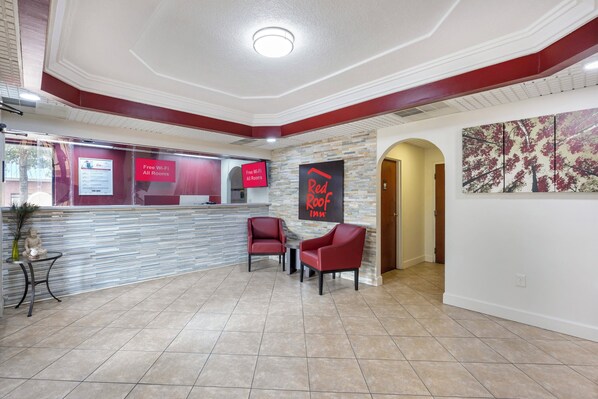 Un hall d’hôtel avec un comptoir d’accueil, deux fauteuils rouges, un mur en pierre et un grand tableau abstrait.