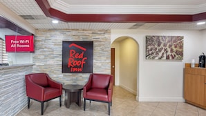 Un hall d’entrée de Red Roof Inn avec un mur en pierre, une enseigne Red Roof, une affiche indiquant que le Wi-Fi est gratuit, deux fauteuils en cuir et une machine à café.