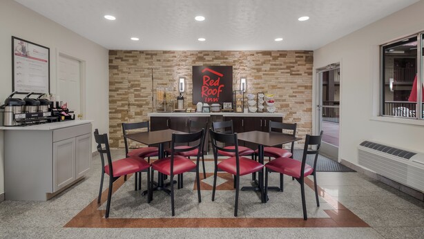 A modern kitchen with a stone backsplash, a central island with a coffee machine, and a dining area with red chairs. - Red Roof Inn Crossville (Crossville)