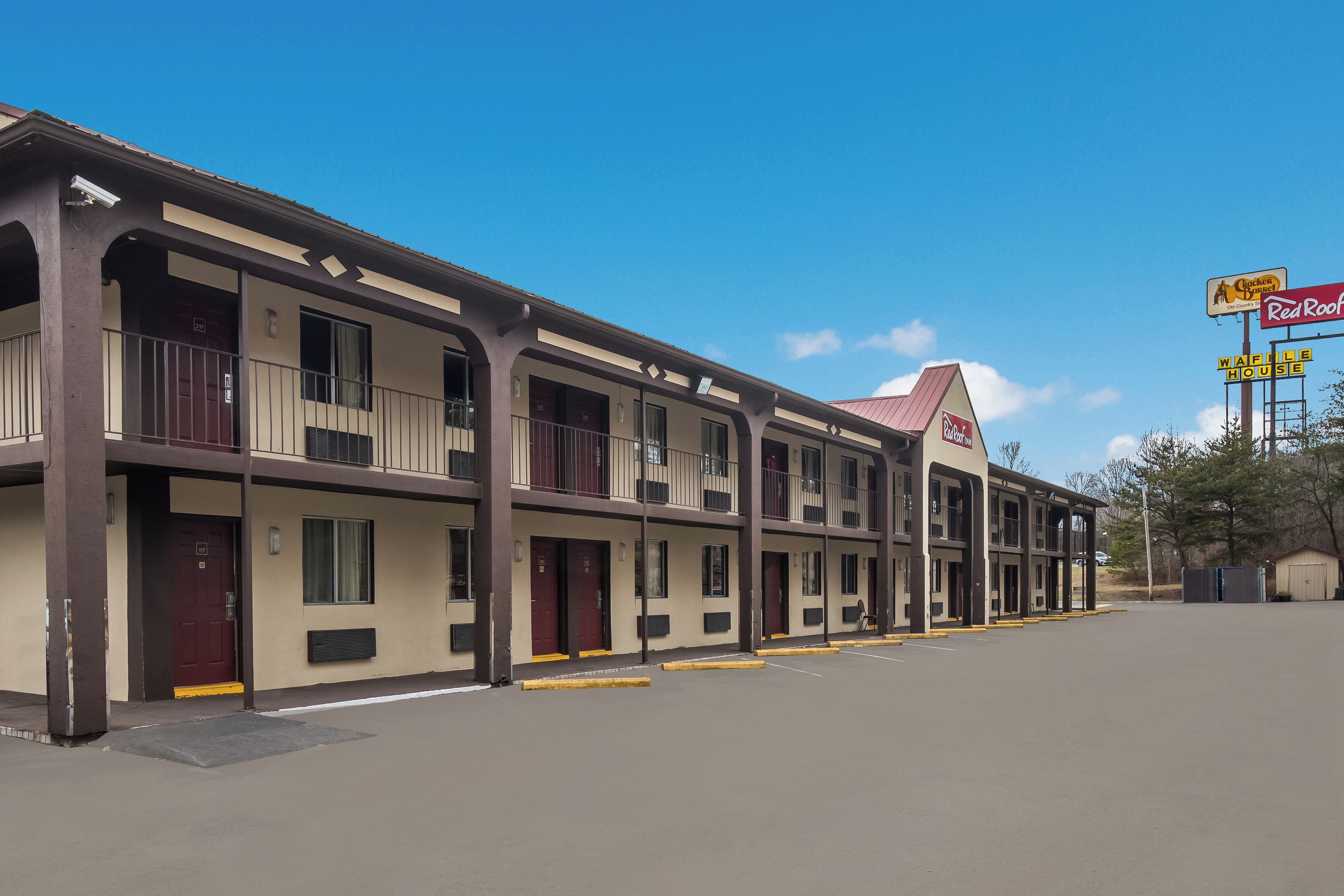 Un motel de varios pisos con fachada plana, varios balcones y un estacionamiento al frente.