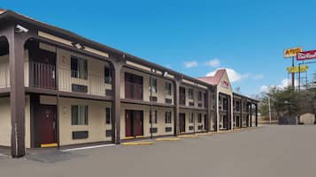 Un motel de varios pisos con fachada plana, varios balcones y un estacionamiento al frente.