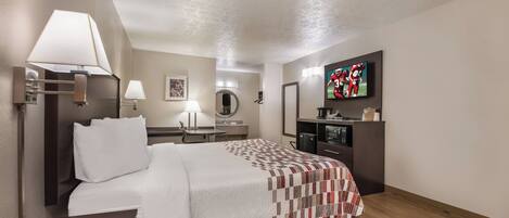 A hotel room with a bed, bedside table, lamp, TV, and a small kitchenette.