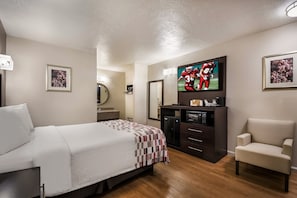 Ein Hotelzimmer mit einem Bett, einem Fernseher, einem Schreibtisch mit Computer, einem Sessel und einem Spiegel.