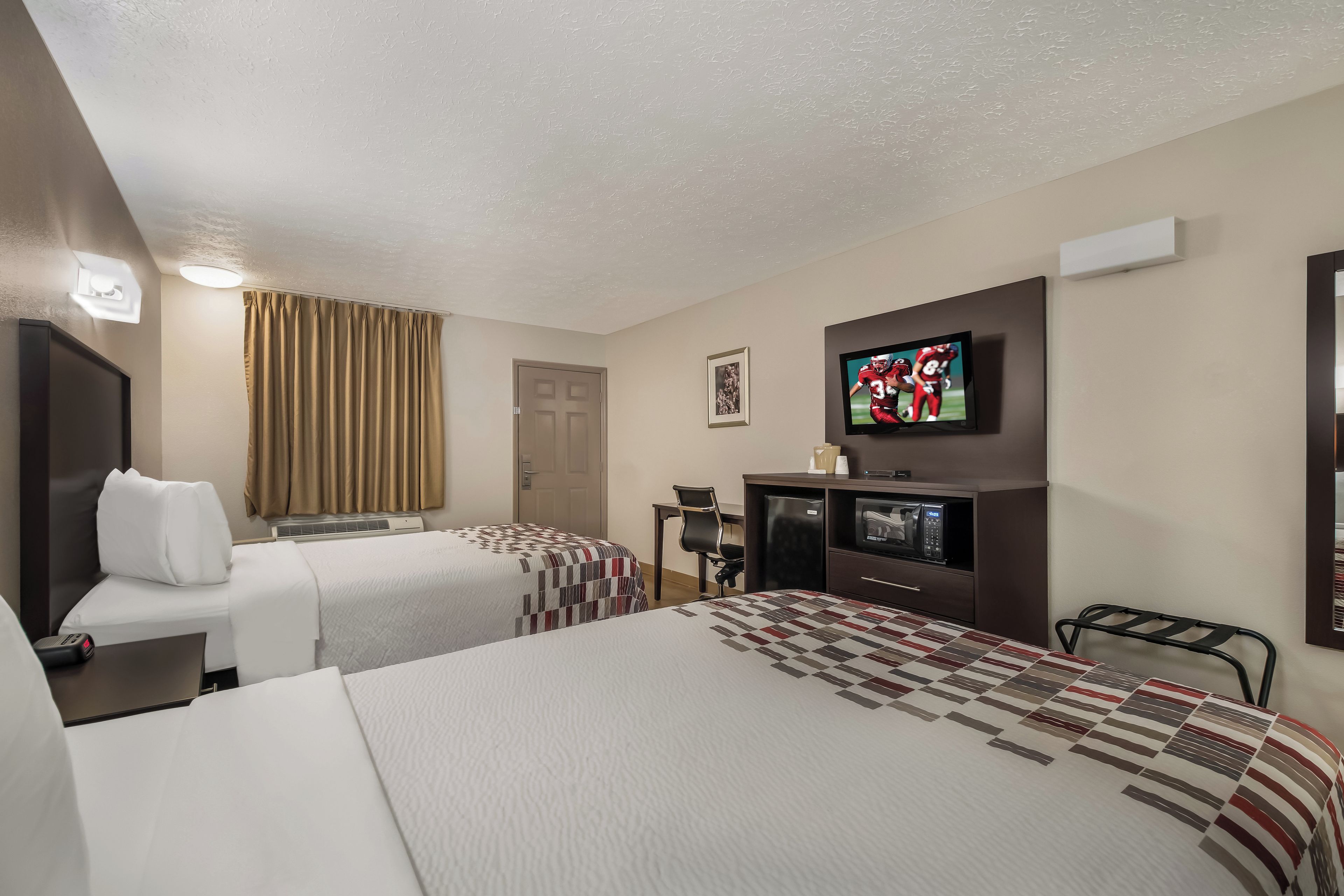 A hotel room with two beds, a television, a desk with a computer, and a microwave.