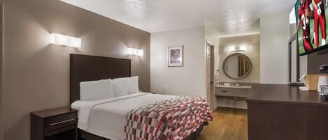 A hotel room with a bed, bedside table, wall-mounted lights, a mirror, and a bathroom with a sink and mirror.