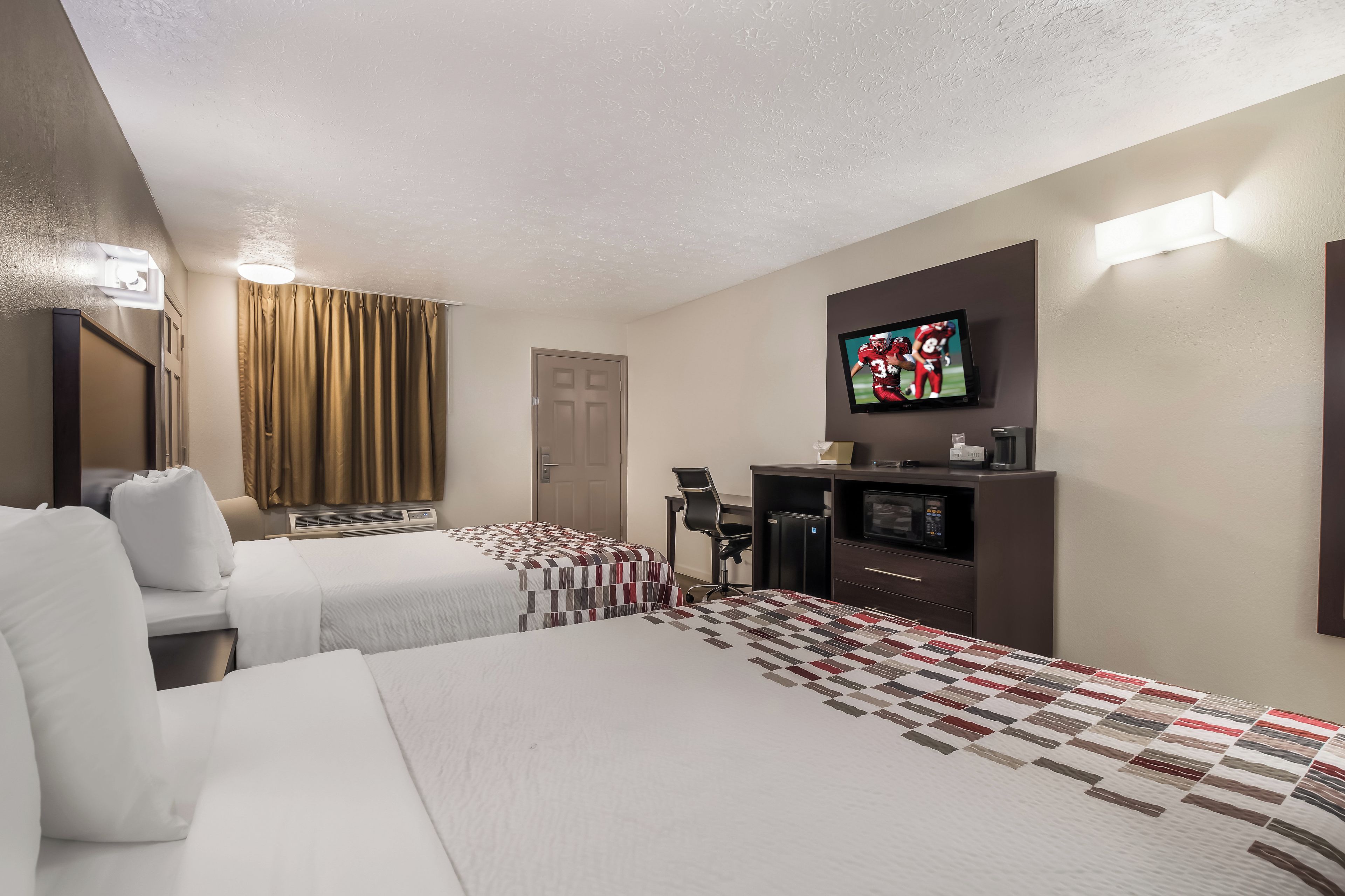 Habitación de hotel con dos camas, televisión, escritorio con silla y minibar.