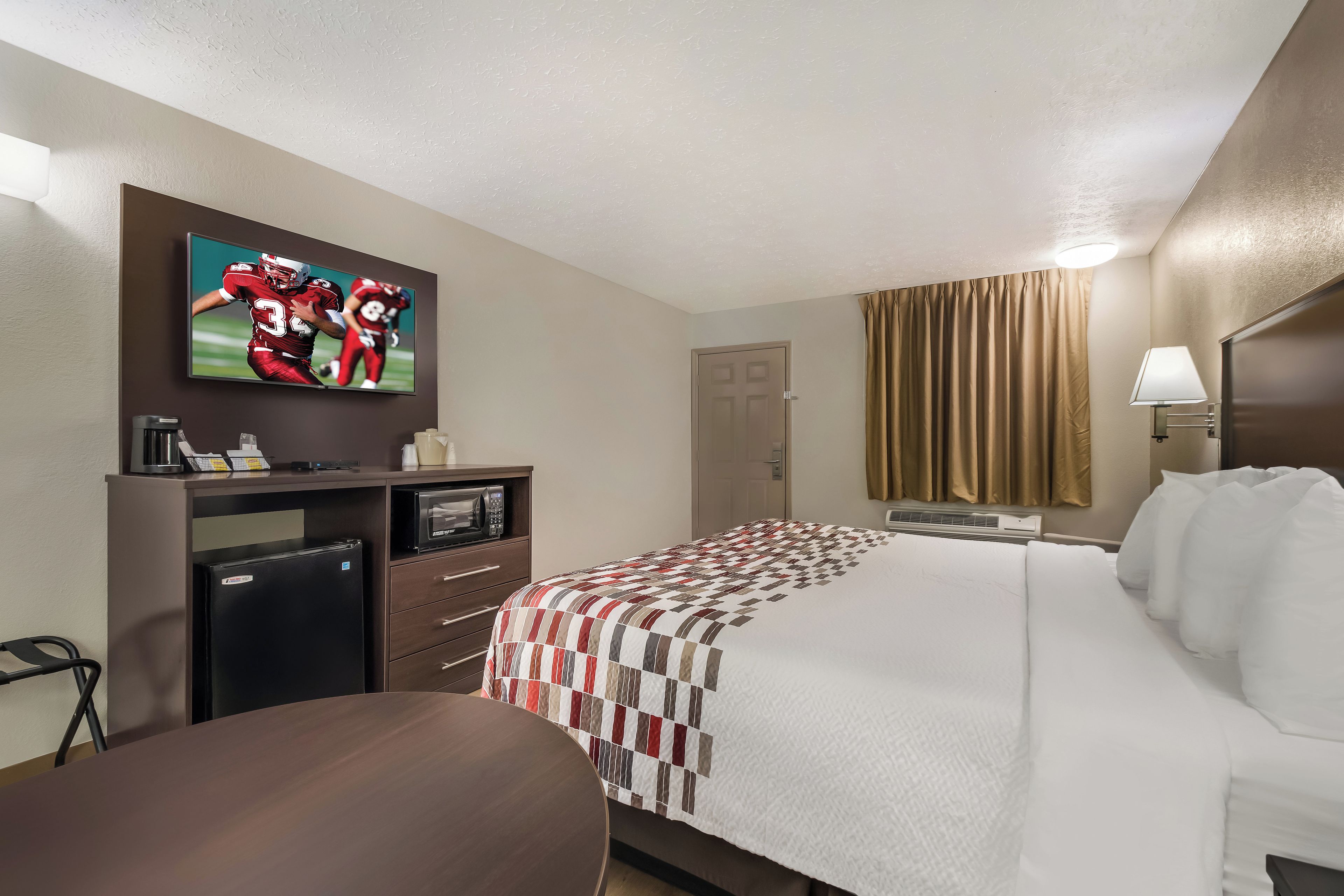 Ein Hotelzimmer mit Bett, Schreibtisch, Fernseher, Mikrowelle und einer Kaffeemaschine.