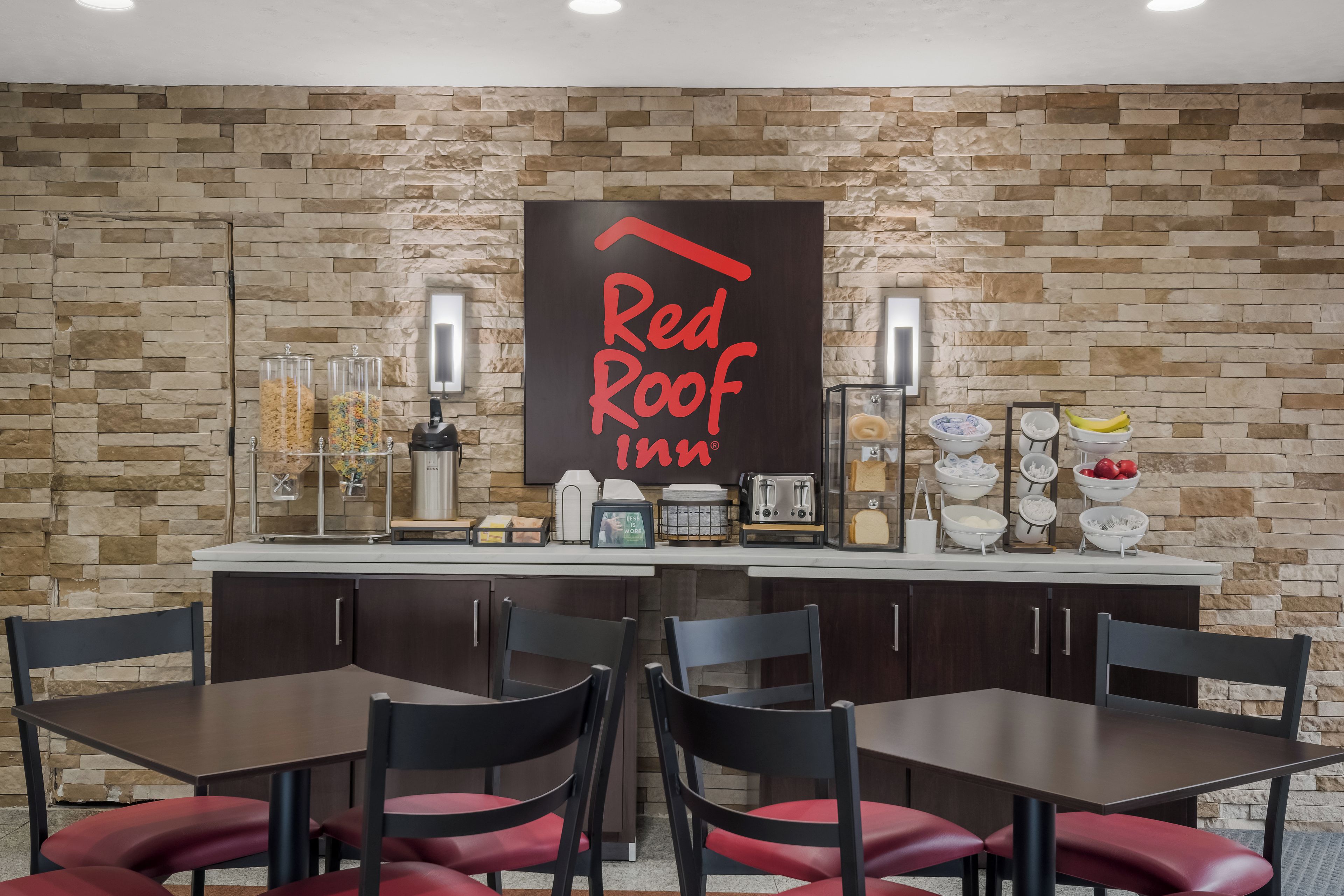 El área de desayuno de Red Roof Inn, con un fondo de pared de piedra, una máquina de café, dispensadores de cereales y un tostador.