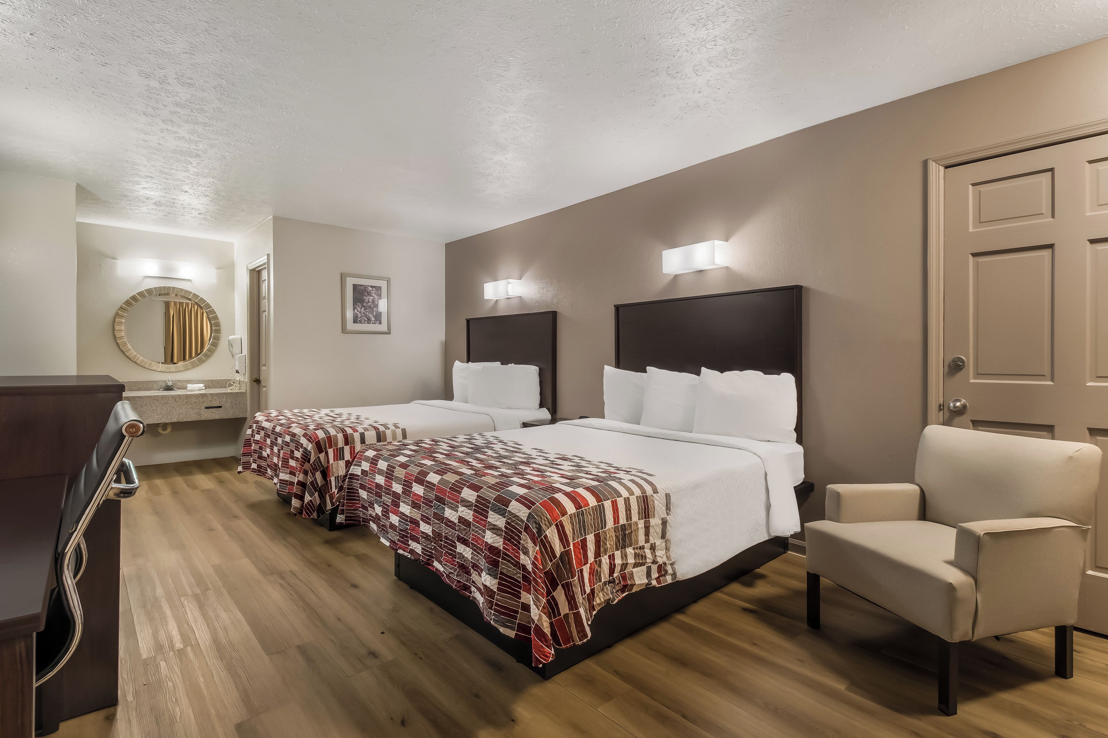 A hotel room with two beds, a desk, a chair, a mirror, and a door.