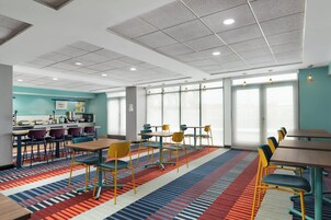 A modern hotel room with a kitchen area, multiple seating arrangements, and large windows providing natural light.