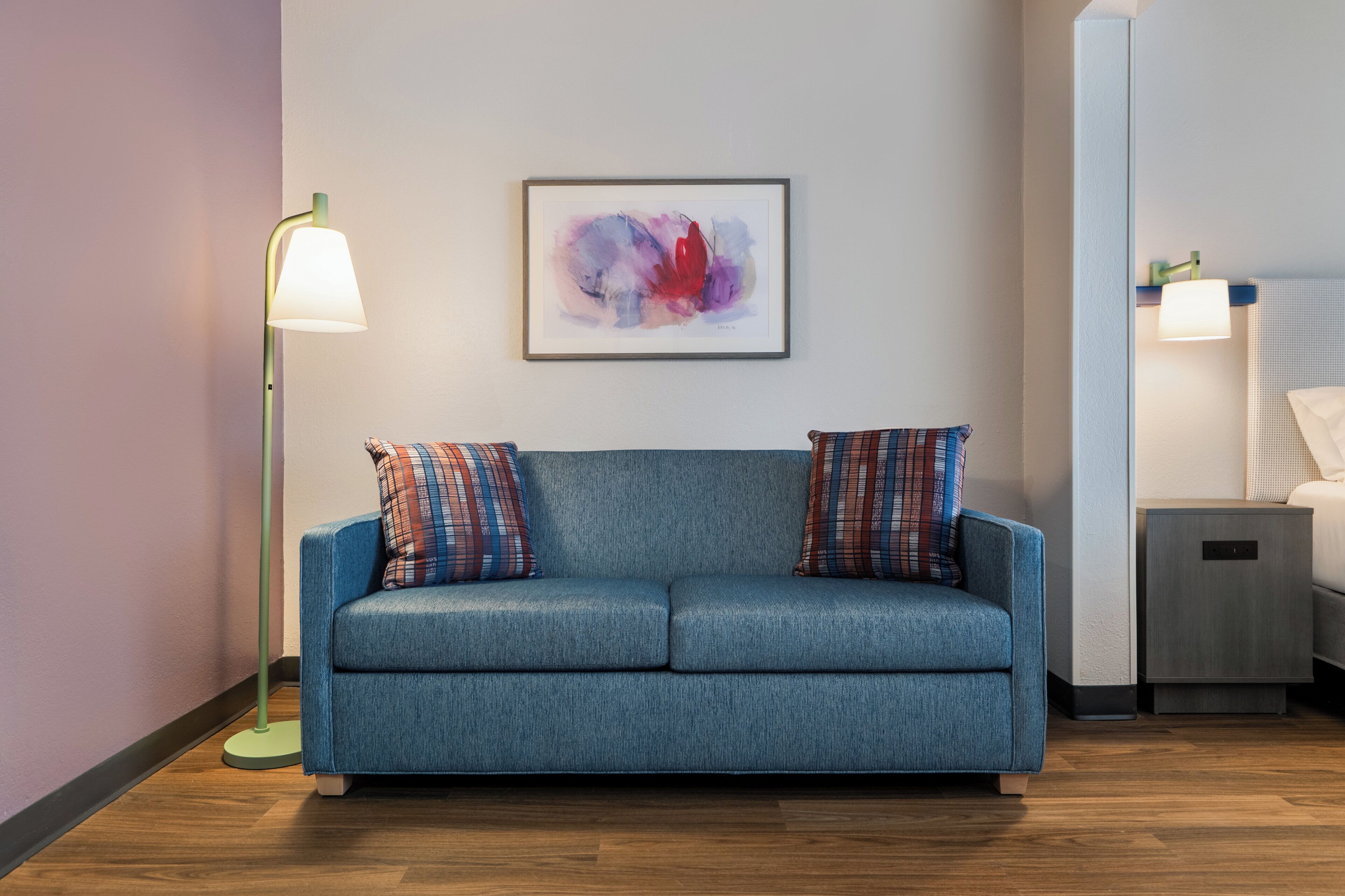 Un sofá azul con almohadones estampados, un cuadro abstracto enmarcado y una lámpara de pie.
