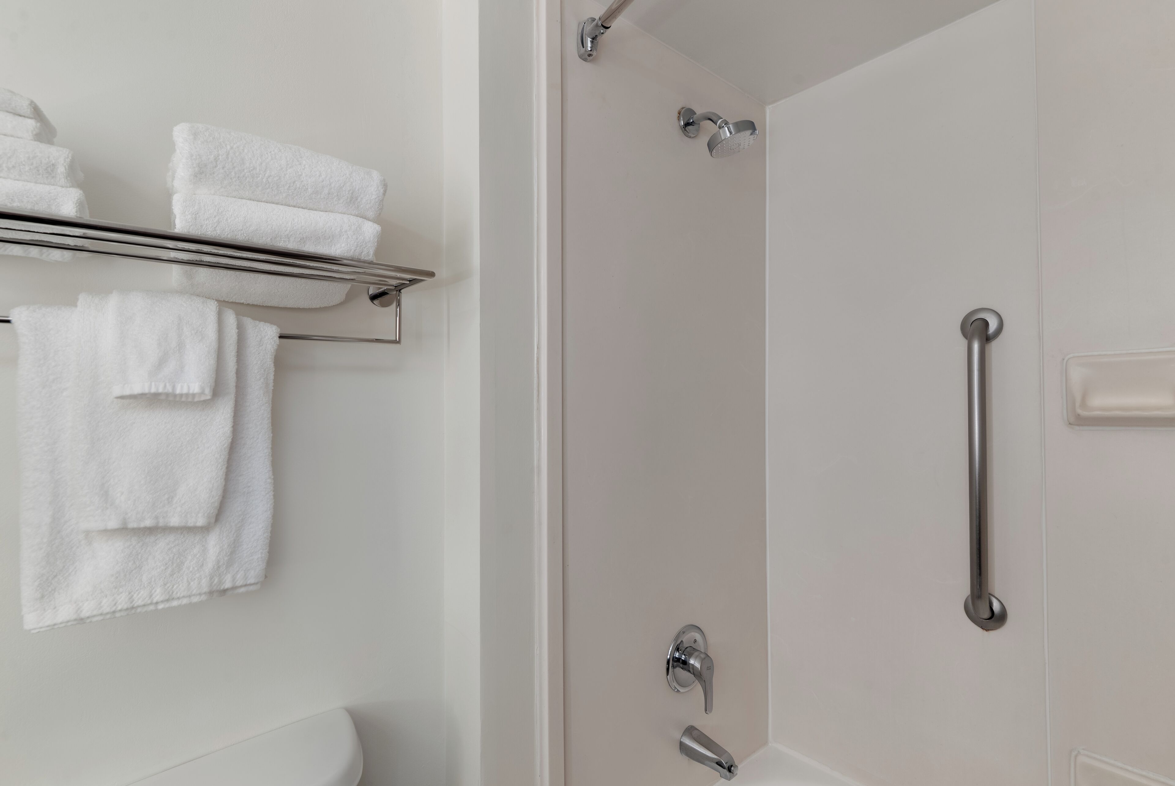 A bathroom with a shower, a toilet, and a towel rack with folded towels.