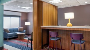 Een hotel lobby met een houten receptiebalie, twee paarse stoelen, een blauwe bank en een kamerbreed tapijt met dessin.