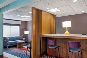 A hotel lobby with a wooden reception desk, two purple chairs, a blue sofa, and a patterned carpet.