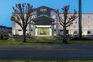 A hotel entrance with a parking lot, a large tree, and a building with a sign reading "Garnier BY IHG".