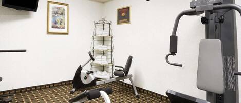 A gym with exercise equipment, a TV, and framed artwork on the walls.