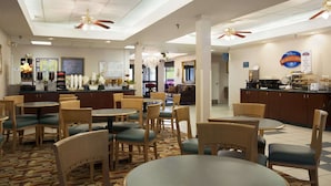 A hotel restaurant with multiple dining tables and chairs, a bar area, and ceiling fans.