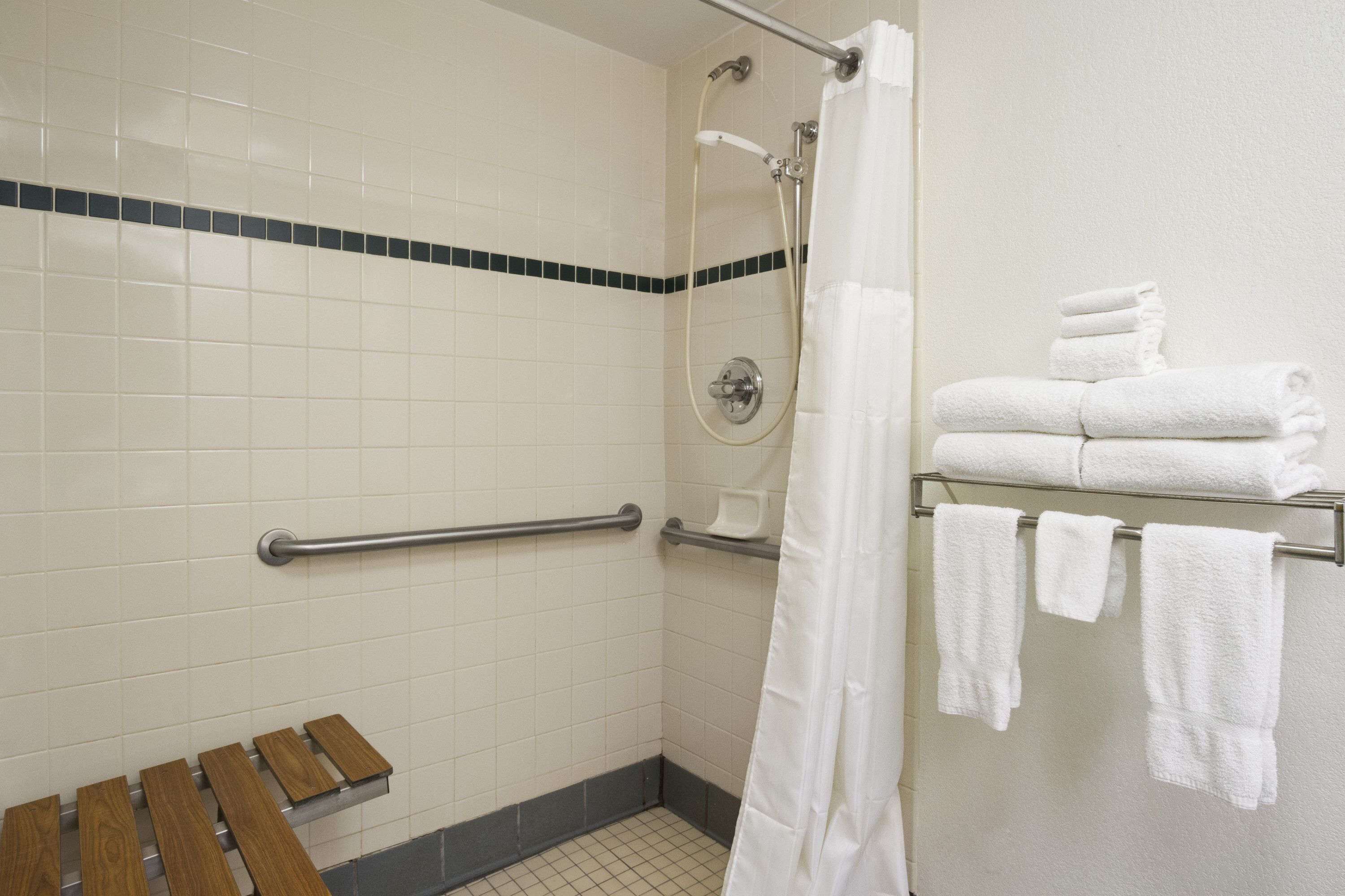 A shower area with a glass door, a handrail, a bench, and a towel rack with towels.