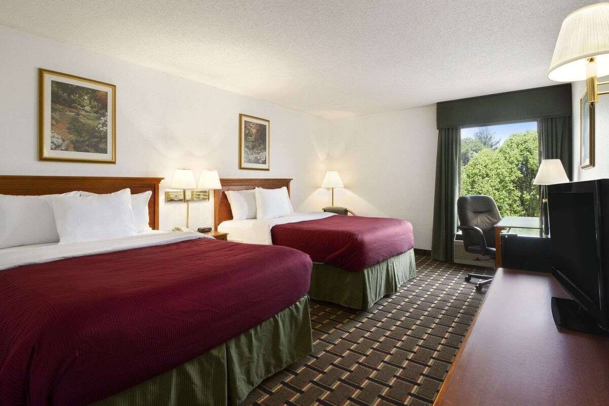 A hotel room with two beds, a desk, a chair, and a TV.
