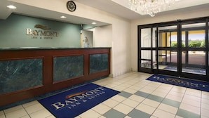 A reception area with a Baymont Inn & Suites sign, a clock, a chandelier, and a view through the glass doors.