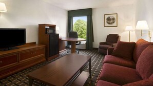 A hotel room with a television, a small refrigerator, a dining table, a sofa, and a chair.