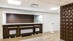 A reception area with a modern design, featuring a reception desk, a wall-mounted information kiosk, and a patterned wall.
