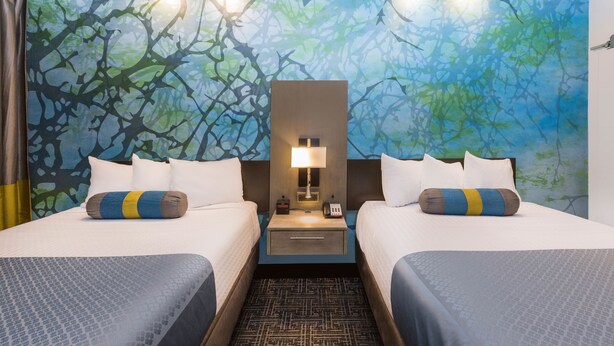 A hotel room with two beds, a nightstand with a lamp, and a wall mural.