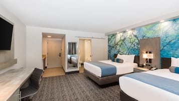 A hotel room with two beds, a desk, a chair, a bathroom, and a large window.