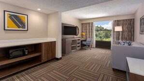 A hotel room with a flat-screen TV, a microwave, a desk, a chair, a sofa, and a window with curtains. - Hampton Inn Bristol (Bristol)